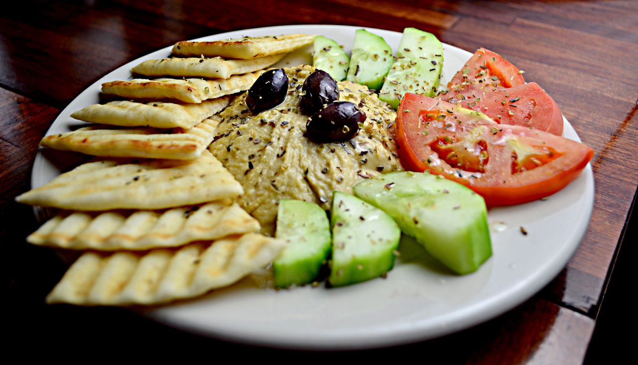Delicious Mediterranean platter featuring hummus, pita, cucumbers, tomatoes, and olives.